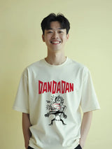 Person wearing a white t-shirt with 'DANDADAN' graphic design on a yellow background